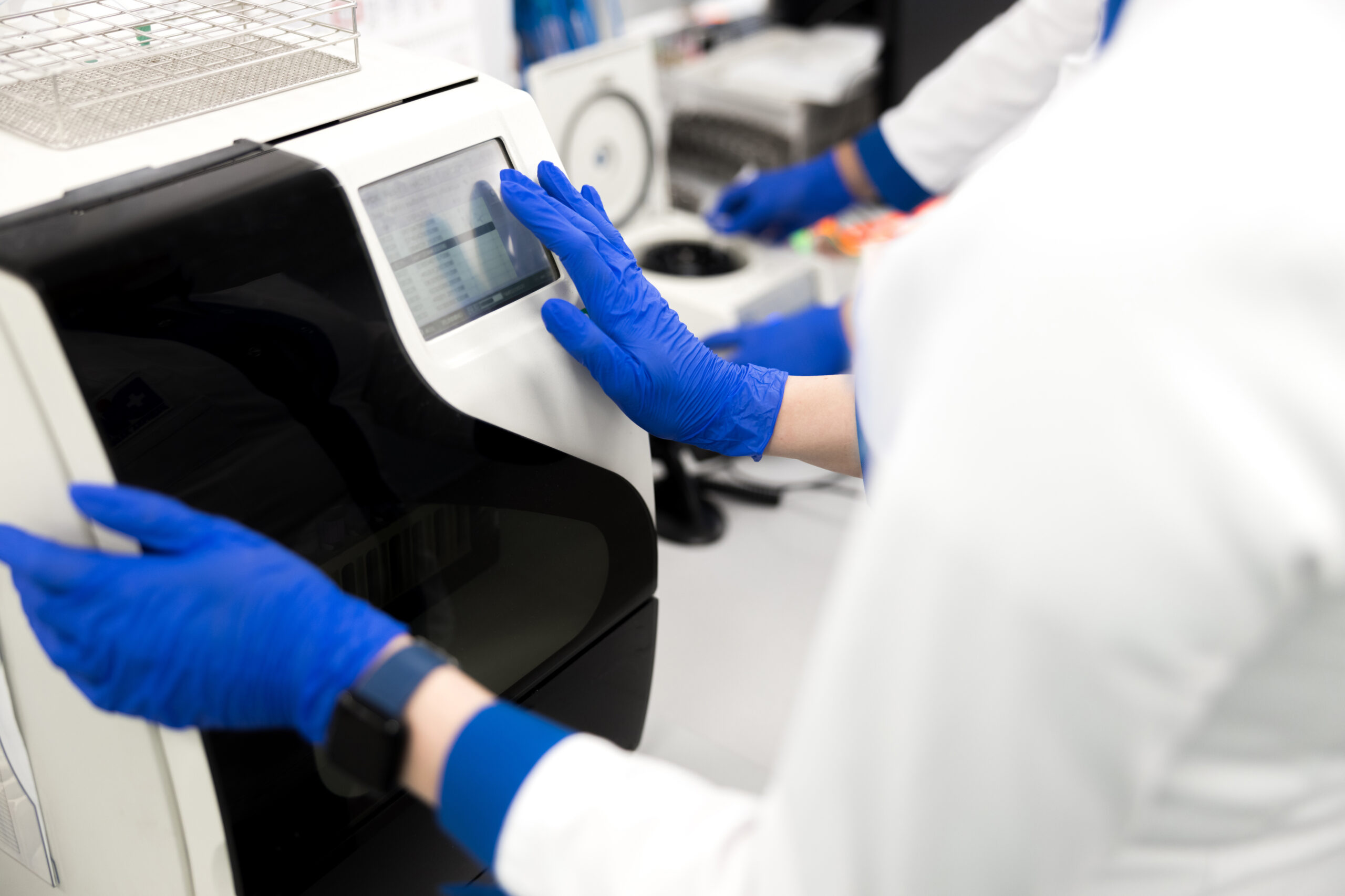 Close up of female hand in sterile glove touching display of lab machine and analyzing results of biochemical blood test stock photo