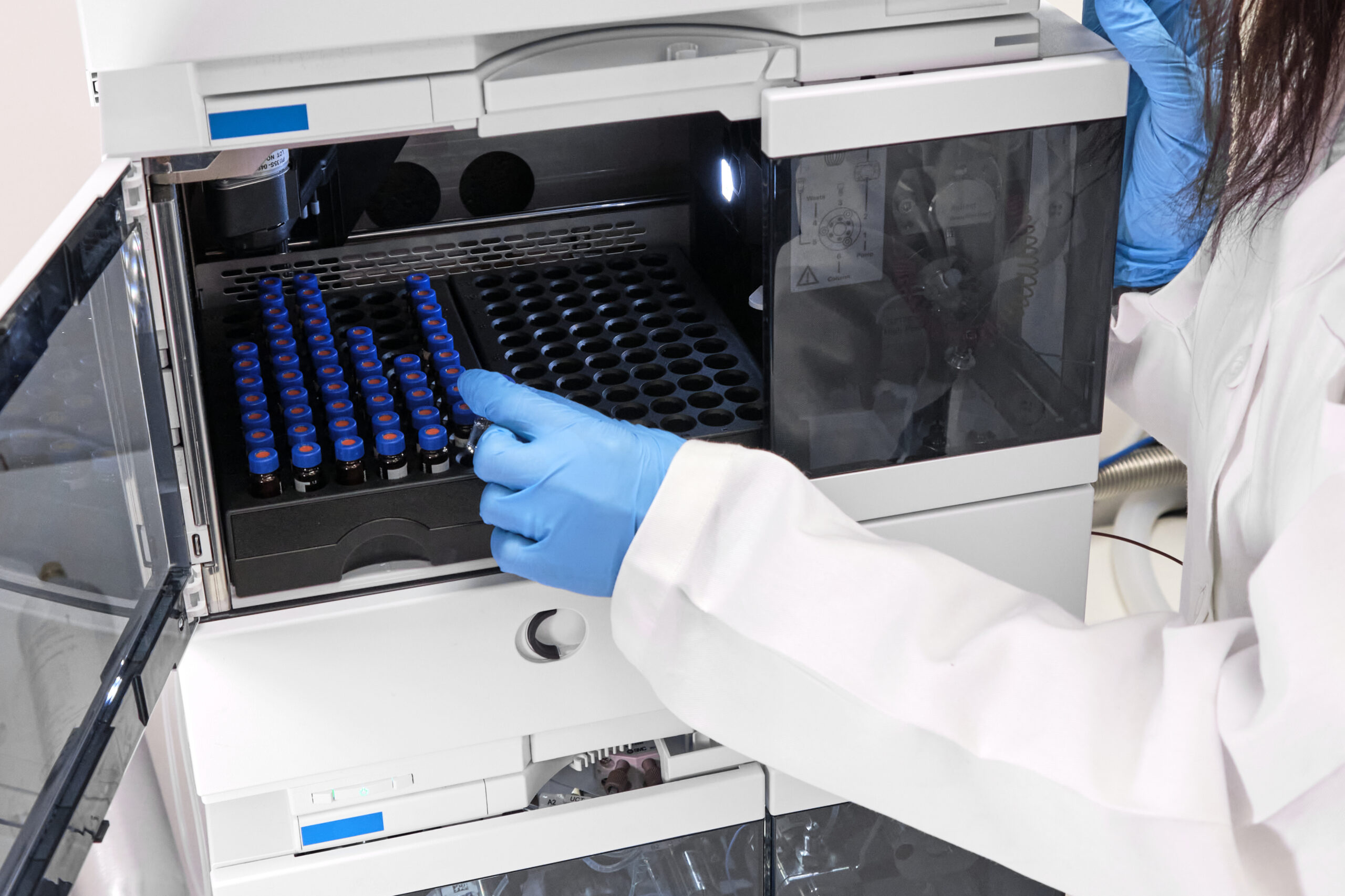 Scientist in a white lab coat putting vial with a sample into autosampler of HPLC system. High performance liquid chromatography at chemical laboratory. Developing of pharmaceuticals or vaccine. Biochemistry analysis